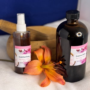 May include: Two brown glass bottles with labels that read "Snatched Body Big mama's helper BMH". The bottles are sitting on a white surface with a single orange lily flower.