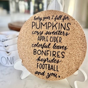 May include: Cork coaster with black text that reads "Every year I fall for PUMPKINS cozy sweaters APPLE CIDER colorful leaves BONFIRES hayrides FOOTBALL and you".