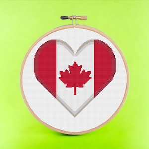 May include: A white heart-shaped cross-stitch with the Canadian flag design. The flag is red and white with a red maple leaf in the center.