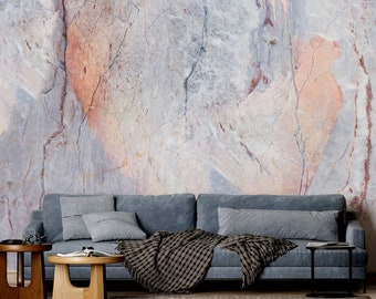 May include: A gray sofa with a black and white throw blanket sits in front of a wall with a marble-like pattern in shades of gray, pink, and brown. A wooden floor lamp with a white lampshade stands to the right of the sofa. Two wooden side tables are in front of the sofa.