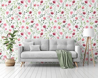 May include: A gray sofa with a green throw blanket sits in front of a white wall with a pink floral pattern. A potted plant and a floor lamp are also in the room.