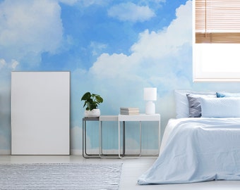 Puede incluir: Un dormitorio con un papel tapiz de nubes azul y blanco, una cama blanca con ropa de cama azul, una lámpara blanca sobre una mesita de noche blanca y un cuadro blanco enmarcado en la pared.