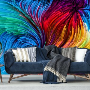 Pu&ograve; includere: Un divano in velluto blu con una coperta di lana grigia e cuscini con motivi colorati si trova di fronte a un murale che presenta un design astratto a spirale di linee colorate.