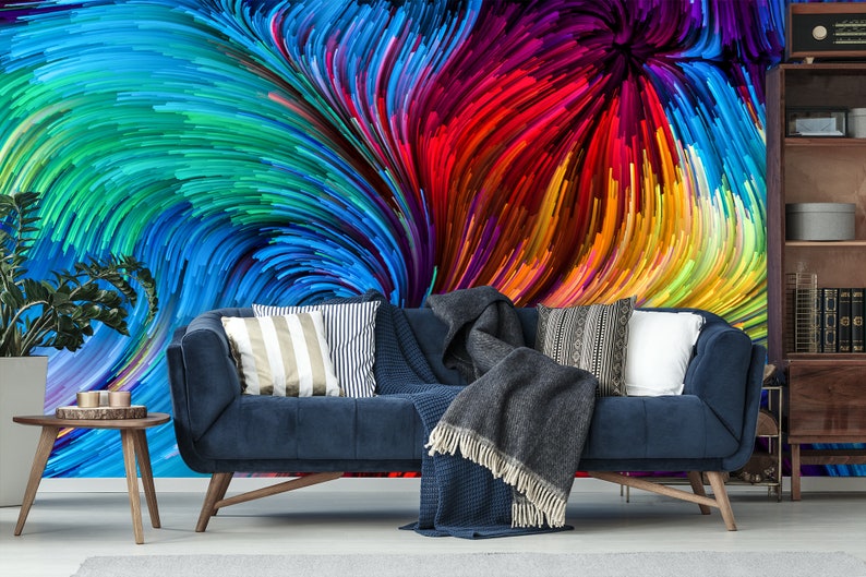 Pu&ograve; includere: Un divano in velluto blu con una coperta di lana grigia e cuscini con motivi colorati si trova di fronte a un murale che presenta un design astratto a spirale di linee colorate.