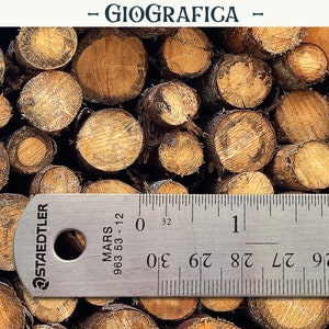 Peut inclure: Gros plan sur une pile de bûches de bois empilées avec une règle en argent mesurant 5 cm de large en haut. La règle est étiquetée "STAEDTLER" et "MARS 963 53-12".
