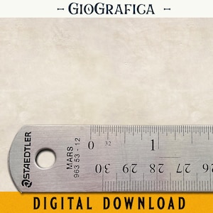 Op de afbeelding: Een zilveren liniaal met zwarte markeringen en de woorden "STAEDTLER" en "MARS 963 53-12" erop gedrukt. De liniaal ligt op een wit oppervlak met de tekst "GIOGRAFICA" erboven.