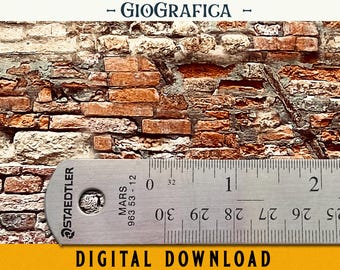 May include: A close-up of a weathered brick wall with a ruler laying across it. The ruler is a silver Staedtler Mars 963 53-12 ruler with black markings. The text "GIOGRAFICA" is visible above the ruler.