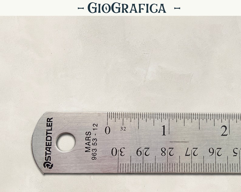 May include: A stainless steel ruler with black markings and the text "STAEDTLER MARS 963 53-12". The ruler measures up to 2 inches and 30/32 of an inch. The word "GIOGRAFICA" is at the top.
