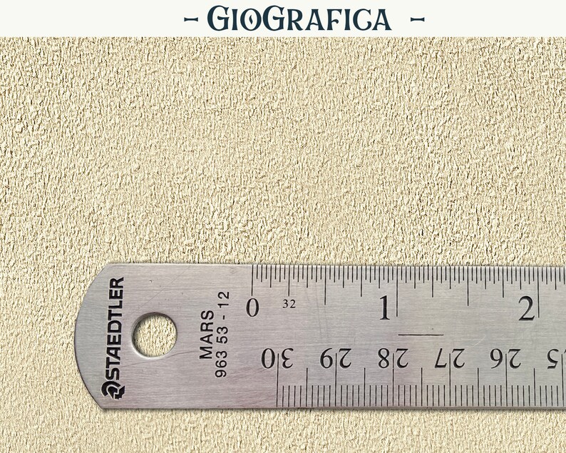 May include: A close-up of a beige textured surface with a metal ruler measuring 2 inches. The ruler is labeled "Staedtler Mars 963 53-12" and has markings for 1/16 inches.