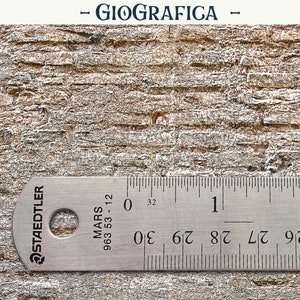 Puede incluir: Primer plano de una superficie texturizada de color marrón claro con una regla para medir. La regla está marcada en centímetros, con el texto "- GIOGRAFICA -" en la parte superior. La regla está marcada con la marca "STAEDTLER".
