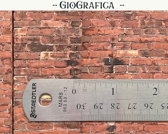 May include: A close-up of a red brick wall with a metal ruler measuring 2 inches. The ruler is labeled "STAEDTLER MARS 963 53-12".