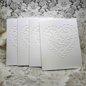 May include: Four white blank cards with an embossed heart design. The heart has a delicate lace pattern.