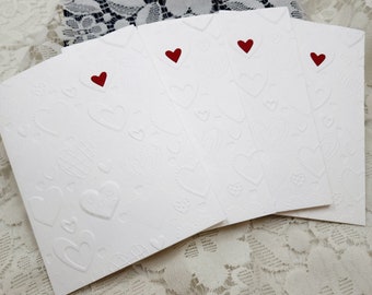 May include: Four white cards with a raised heart pattern and a red heart in the center of each card.
