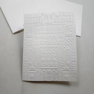 May include: White embossed card with a birthday theme. The card features the text "Happy Birthday to you" and various birthday-related illustrations, including presents, balloons, candles, and a cake.