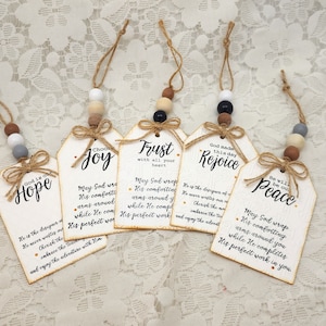 May include: Five wooden tags with inspirational quotes about hope, joy, trust, rejoice, and peace. Each tag is decorated with a brown twine bow and a string of wooden beads in various colors.