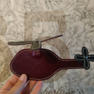 May include: A burgundy leather helicopter keychain with a gray propeller and black tail rotor.