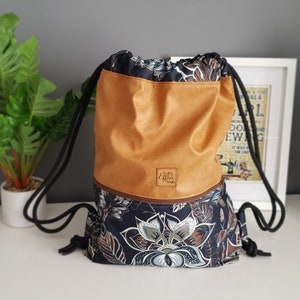 May include: A brown and black drawstring bag with a floral pattern. The bag has a brown leather flap with a zipper and a small leather tag that says "Effika Crafts".