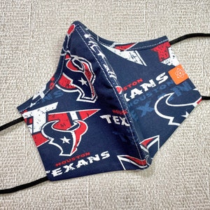 May include: A blue face mask with a white and red Houston Texans logo pattern. The mask has black elastic ear loops.
