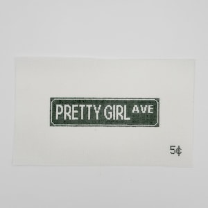 May include: A white canvas with a green street sign that reads "PRETTY GIRL AVE" in white letters. The number "5¢" is printed in black on the lower right corner. The canvas has a grid-like texture.