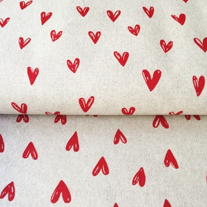 May include: A close-up of a white fabric with a repeating pattern of red hearts. The fabric is folded in half, showing the pattern on both sides.