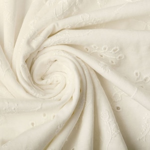 Pode incluir: Tecido de algodão branco com um padrão floral bordado. O tecido é tecido com pequenos furos, criando um visual arejado e delicado.