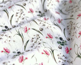 May include: White fabric with a floral pattern featuring pink flowers, green leaves, and small white blossoms. The fabric has a slightly wrinkled texture, suggesting a natural material like linen or cotton. The design is delicate and botanical.