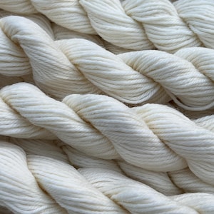 May include: Close-up of several thick, off-white yarn ropes. The ropes are tightly twisted, creating a textured surface. The yarn appears soft and fluffy, suggesting a natural fiber. The image highlights the texture and color of the yarn, suitable for crafting projects.