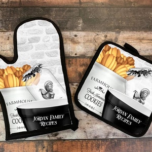 Peut inclure: Un ensemble de deux maniques de four noir et blanc sur le thème de la ferme. Les maniques présentent un fond blanc avec un motif de mur de briques, un bocal de biscuits et un coq. Le texte "Farmhouse Fresh Homemade Cookies" et "Jordan Family Recipes" est imprimé sur les maniques.