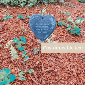 May include: A black heart-shaped slate garden marker with the text "I'll hold you in my heart until I can hold you in my arms" and the date "2.8.2020". The marker is on a metal stake and is surrounded by red mulch.