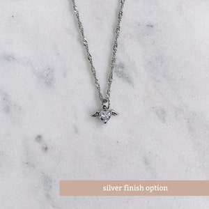 May include: A silver necklace with a heart-shaped pendant, small wings, and a clear gemstone. The chain has a twisted rope design. The image includes the text "silver finish option" at the bottom.