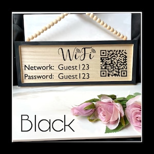 May include: Black wooden sign with a white background and black text that reads "WiFi" with a QR code. The sign also includes the text "Network: Guest123" and "Password: Guest123". The sign is hanging from a string of wooden beads.