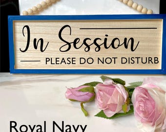 May include: A wooden sign with a blue frame that reads "In Session - Please Do Not Disturb". The sign is painted in a royal navy blue color.