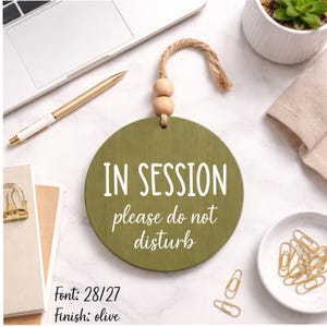 May include: Olive green wooden sign with the words "IN SESSION please do not disturb" in white. The sign is round and has a jute rope for hanging. The font is 28/27. The finish is olive.