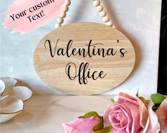 May include: A wooden oval sign with the text "Valentina's Office" in black cursive lettering. The sign is hanging from a string of wooden beads.
