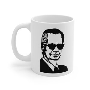 May include: White ceramic mug with a black and white silhouette of a man wearing sunglasses.