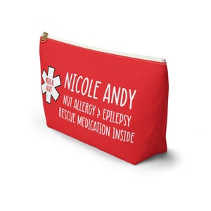 May include: Red zippered pouch with a white medical alert symbol, the text "Nicole Andy", and the words "Nut Allergy & Epilepsy Rescue Medication Inside".
