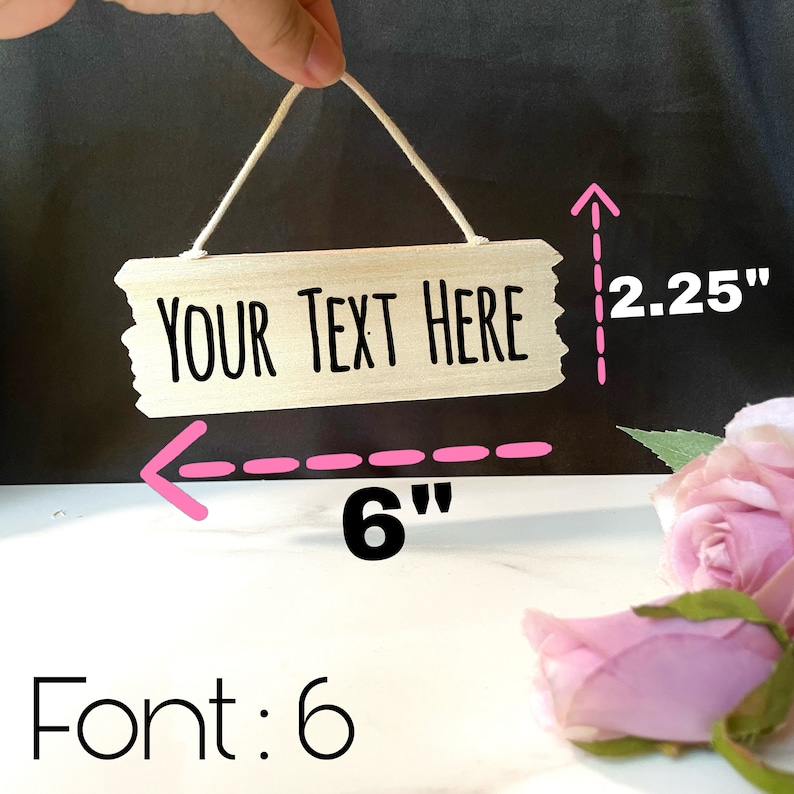 May include: A wooden sign with the text "YOUR TEXT HERE" in black lettering. The sign is 6 inches wide and 2.25 inches tall. The sign is hanging from a string.