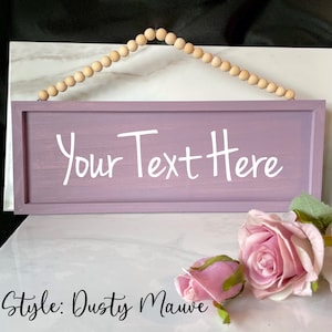 May include: A rectangular, dusty mauve wooden sign with the text "Your Text Here" in white script. The sign is suspended by a string of wooden beads. The words "Style: Dusty Mauve" are written below the sign.