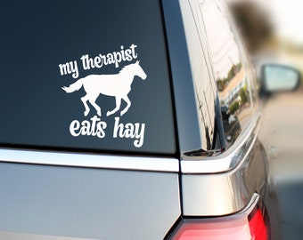 May include: White vinyl decal with a silhouette of a horse running and the text "my therapist eats hay".