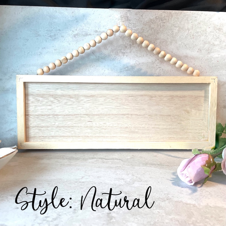 Peut inclure: Panneau rectangulaire en bois clair avec un cadre en bois naturel. Il est suspendu par une guirlande de perles en bois. Le texte "Style: Natural" est &eacute;crit en cursive en bas.