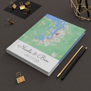 May include: A white notebook with a map of the Seattle, Washington area on the cover. The notebook has the text "Nicole & Ben" and "06.07.23" printed on the front.