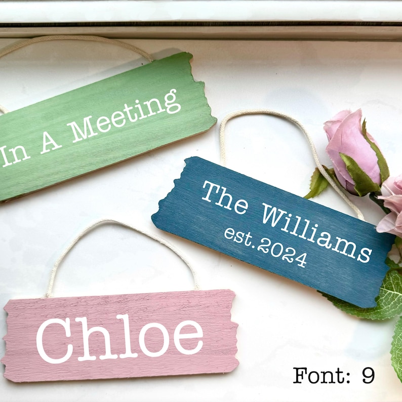 May include: Three wooden signs with distressed paint and white text. The signs are hanging from twine and read "In A Meeting", "The Williams est. 2024", and "Chloe".