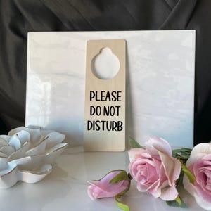 May include: A wooden door hanger with a round hole at the top and the text "PLEASE DO NOT DISTURB" in black lettering.