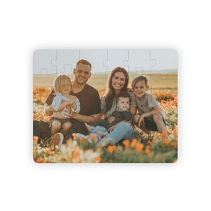May include: A rectangular puzzle featuring a family portrait. The image shows a family of five sitting in a field of orange flowers. The puzzle is white with a glossy finish, and the pieces are interlocked.