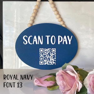 May include: A blue oval sign with white text that reads "SCAN TO PAY" and a black and white QR code. The sign is hanging from a string of wooden beads.