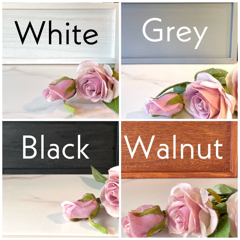 May include: Four wooden signs with different paint colors: white, grey, black, and walnut. Each sign has the color name written in white text. Pink roses are placed in front of each sign.