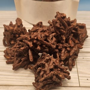 May include: A close-up of a pile of chocolate-covered chow mein noodles. The noodles are arranged in a random pattern and are covered in a thick layer of dark chocolate. The chocolate is shiny and smooth, and the noodles are visible through the chocolate.