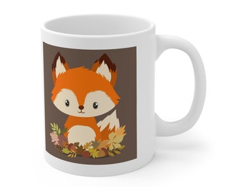 May include: White ceramic mug with a cartoon fox design. The fox has orange and white fur and sits against a brown backdrop. Autumn leaves in brown, yellow, and pink surround the fox. The mug has a curved handle.