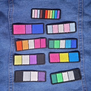 May include: A collection of colorful rectangular patches with a black border, each featuring a different color palette. The patches are arranged on a blue denim jacket. The color schemes include pink, blue, green, yellow, and purple.