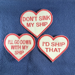 May include: Three white heart-shaped patches with red embroidered borders. The patches have the following text: "Don't Sink My Ship", "I'll Go Down With My Ship", and "I'd Ship That".